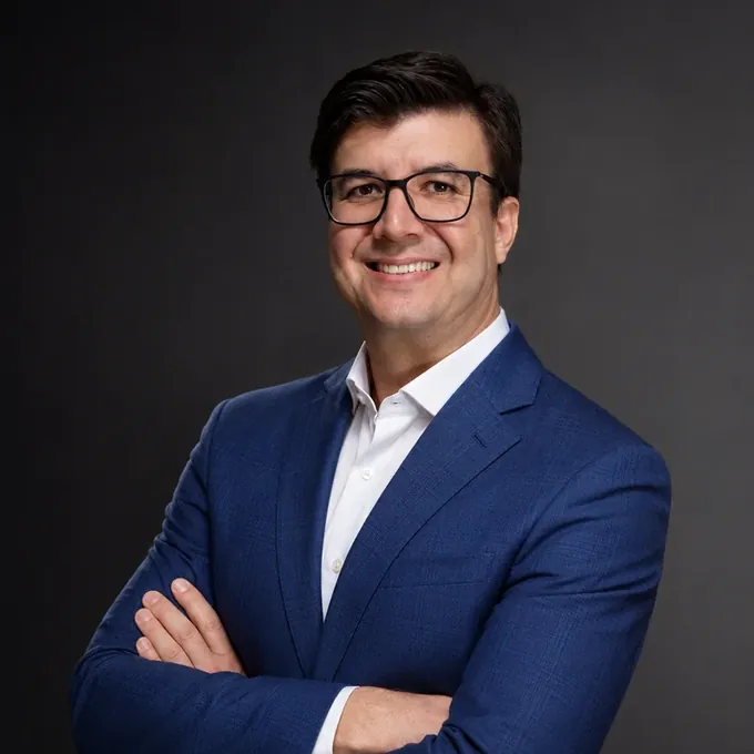 Johnis Pastori de terno azul e braços cruzados, em retrato de estúdio
